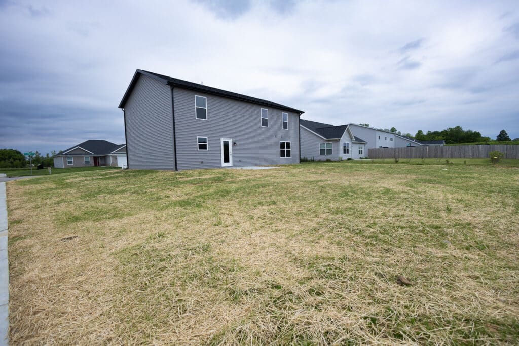 Spacious backyard view showcasing newly built homes and lush green grass.
