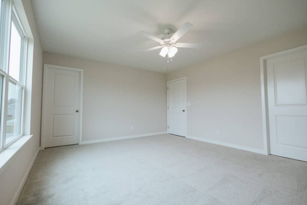 Bright, empty room featuring a ceiling fan and large windows for natural light.