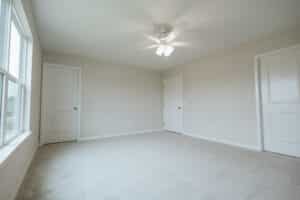 Bright, empty room featuring a ceiling fan and large windows for natural light.