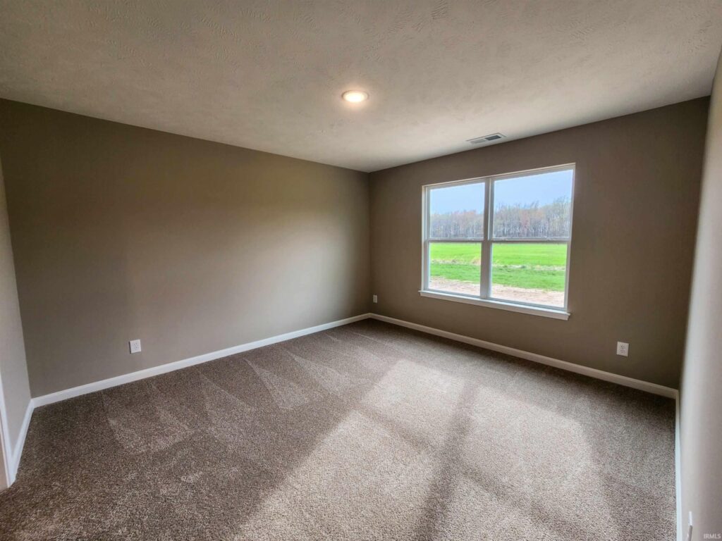 Bright, empty room with a large window overlooking a green field.