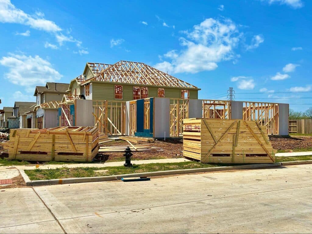 Construction of a wooden frame house progressing under clear, sunny skies.