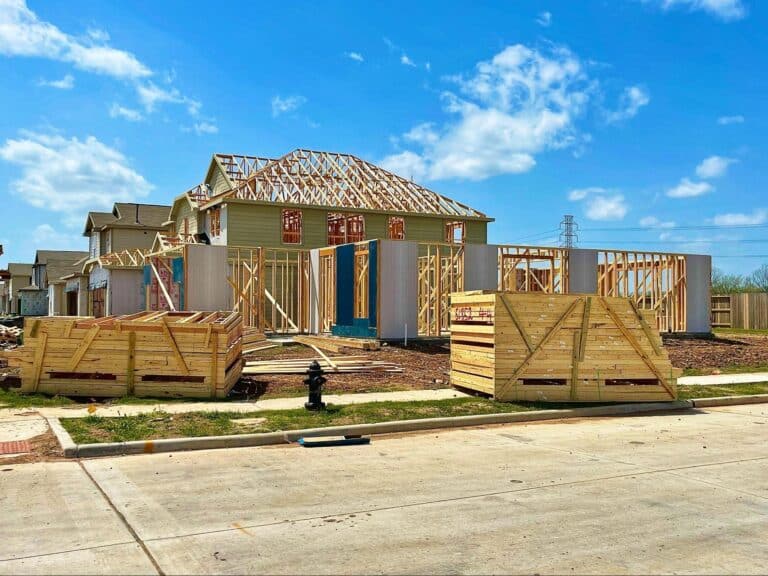 Construction of a wooden frame house progressing under clear, sunny skies.