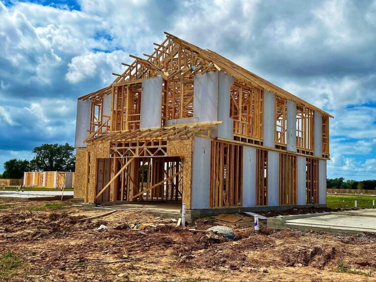 New home construction framing under a cloudy sky in an open area.