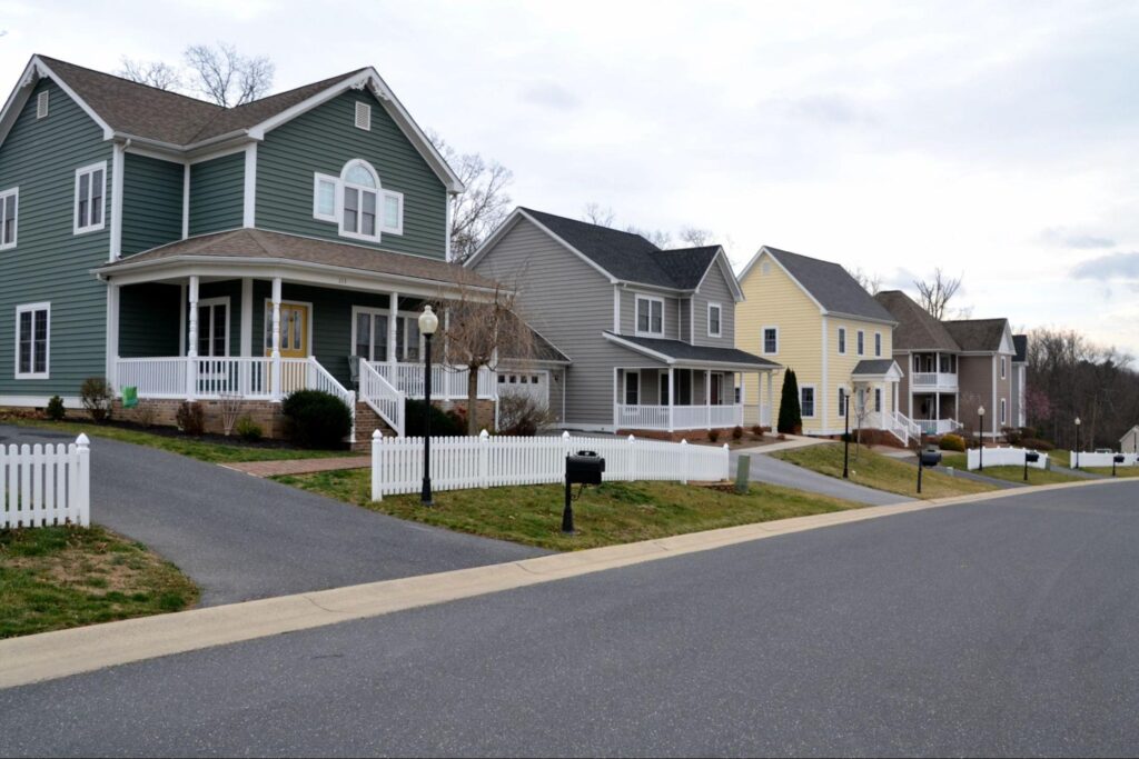 Charming homes line a scenic suburban street with lush lawns and white fences.