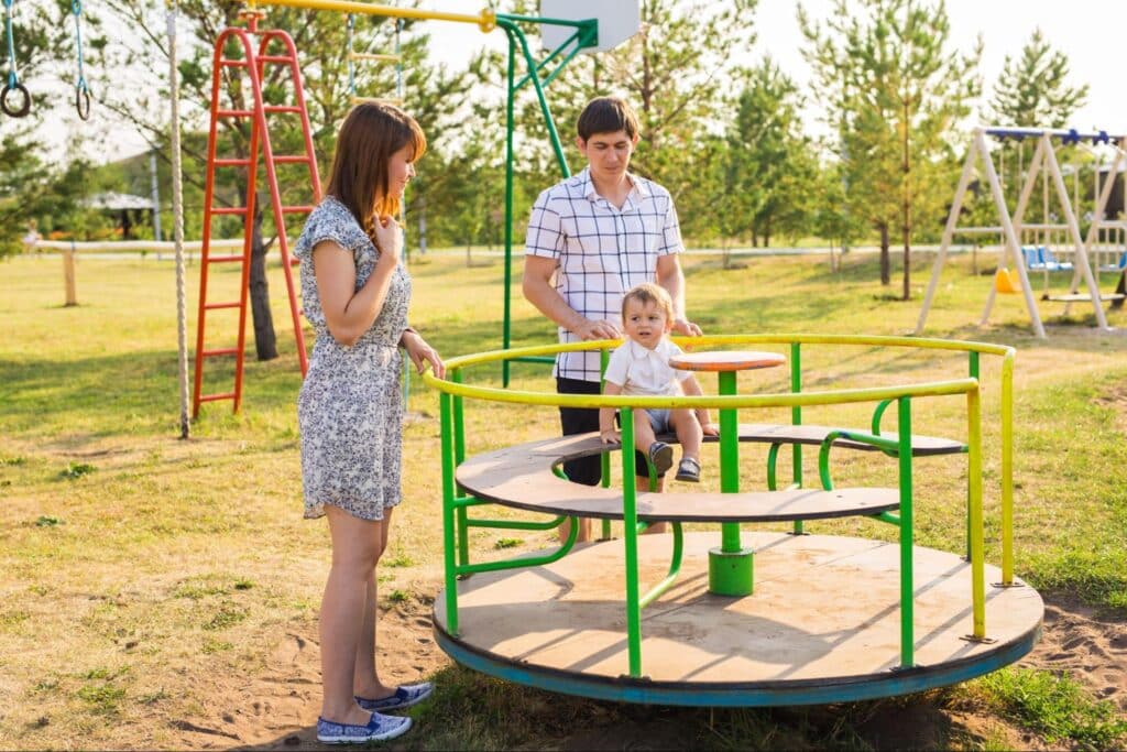 Family enjoying a sunny day at the playground on a merry-go-round.
