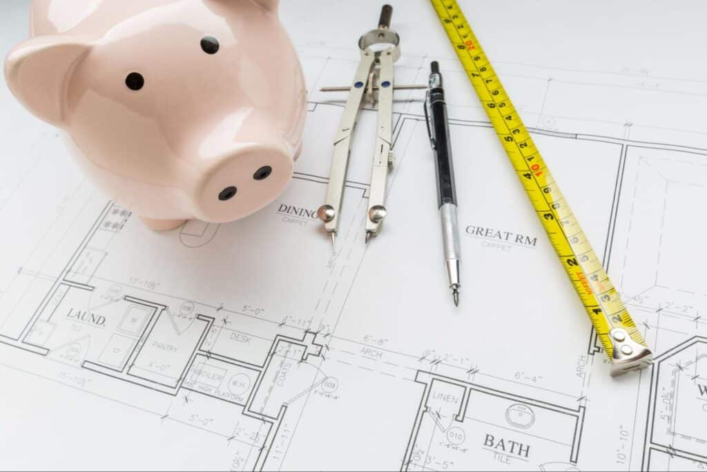 Piggy bank and drafting tools on home design blueprints for budget-friendly planning.