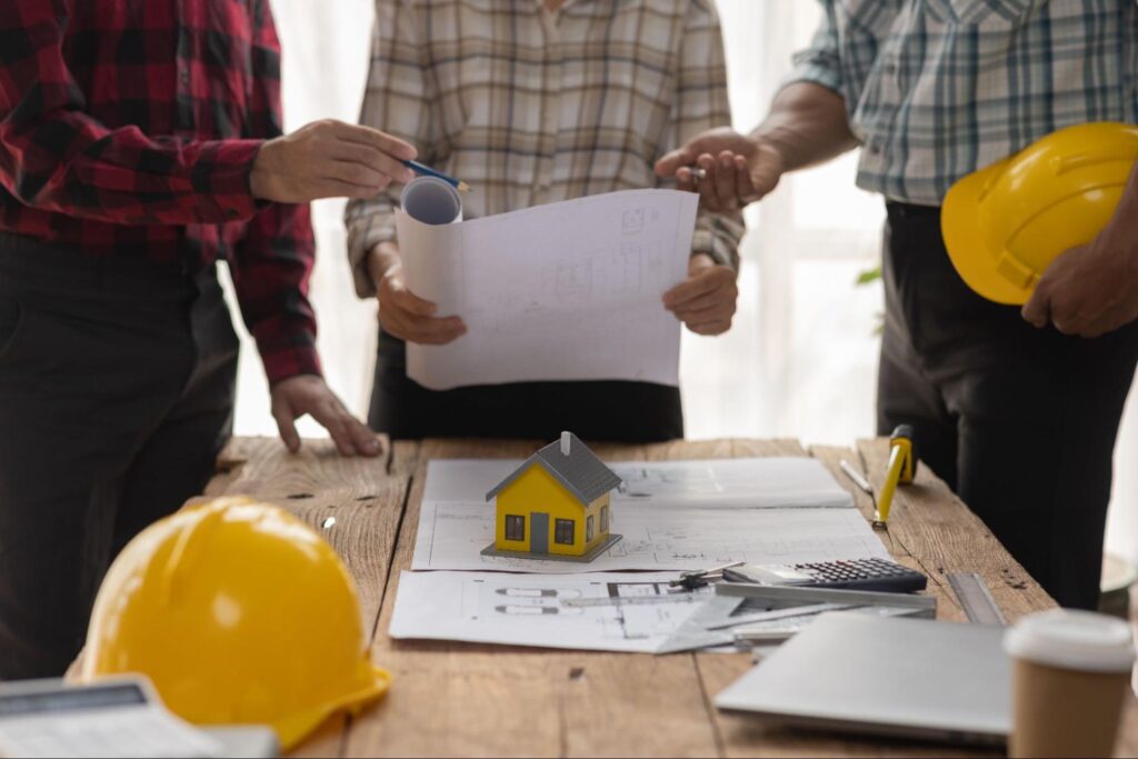 Construction team collaborating on blueprints with a model house at the table.