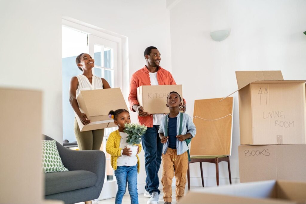 Family joyfully moving into their new home with boxes and plants.