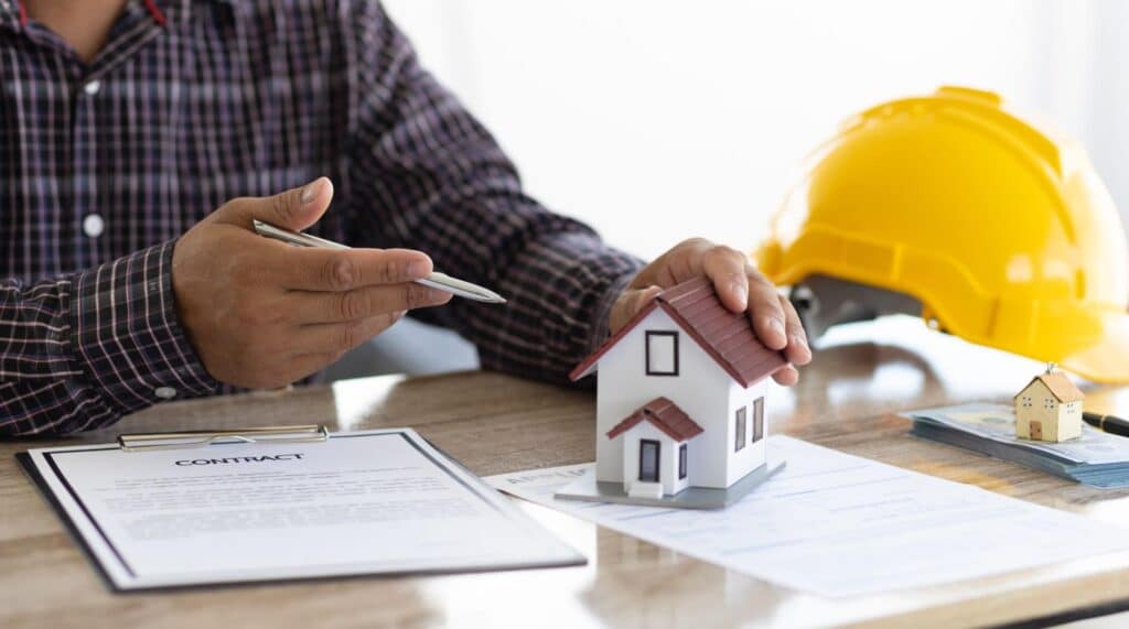Discussing real estate contracts with a model house and construction helmet on the table.