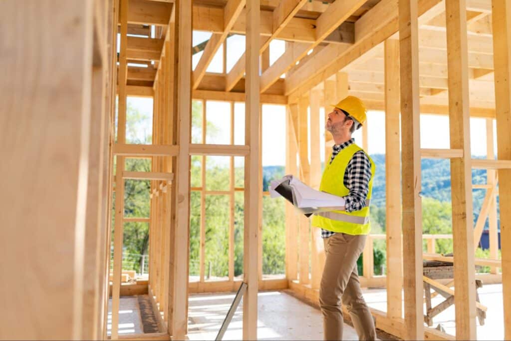 Construction worker reviewing blueprints in a framed building under construction.
