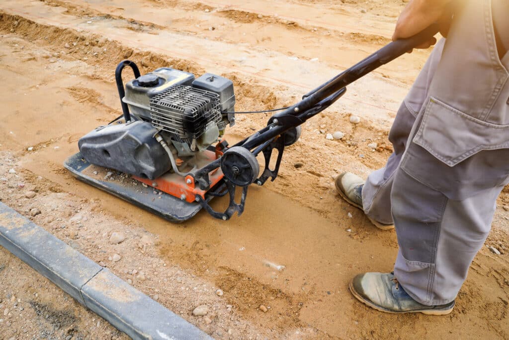 Operator using a tamping machine for compacting soil on a construction site.
