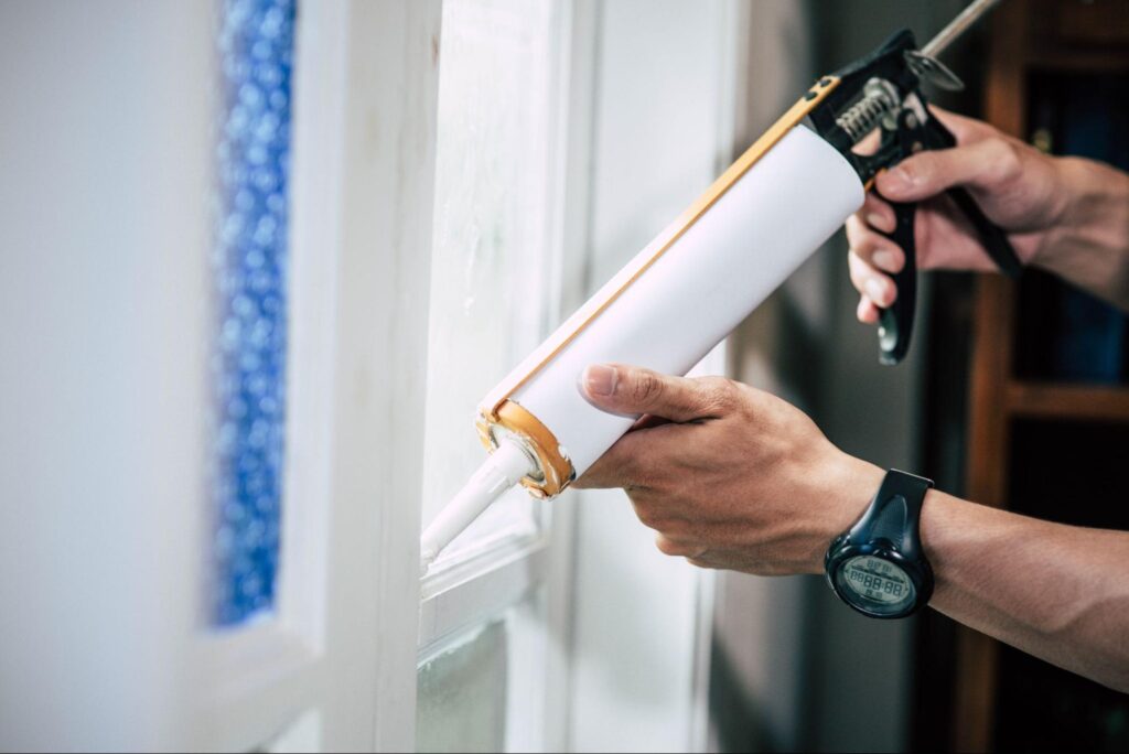 Sealing windows with caulk to enhance energy efficiency in your home.