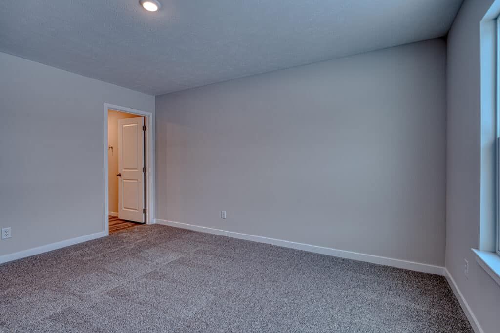 Bright, neutral empty room with open door and carpeted flooring, perfect for various uses.