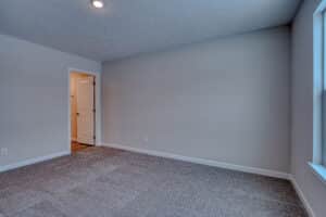 Bright, neutral empty room with open door and carpeted flooring, perfect for various uses.