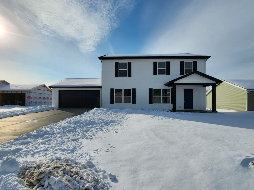 Newly built home surrounded by snow under a bright blue sky.