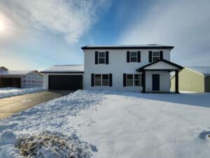 Newly built home surrounded by snow under a bright blue sky.