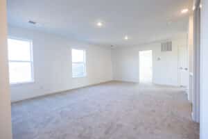 Spacious, empty living room with natural light and plush carpet flooring.
