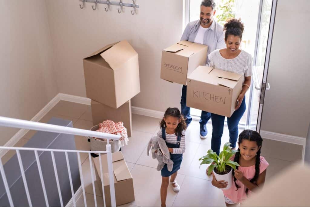 Family joyfully moving into a new home with boxes and a plant.