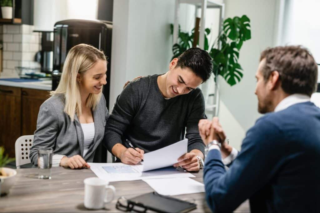 Couple happily signing a new agreement with a professional advisor at a business meeting.