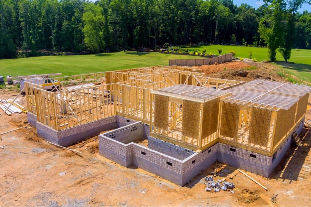 Wooden framing of a new home under construction surrounded by greenery.