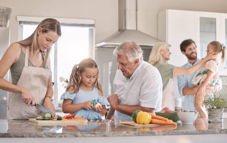 Family cooking together in the kitchen, featuring children, parents, and grandparents preparing vegetables.