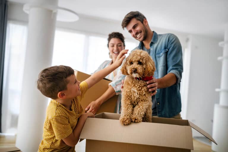 Family joyfully unpacks boxes in their new home with a playful dog.
