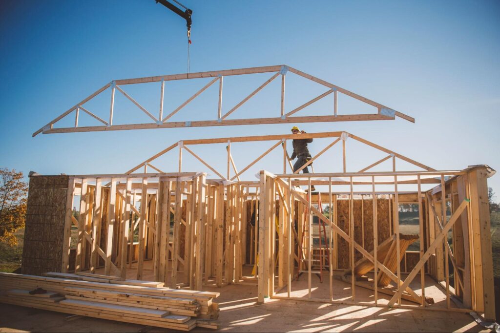 Wood frame construction site with workers assembling a house under blue skies.