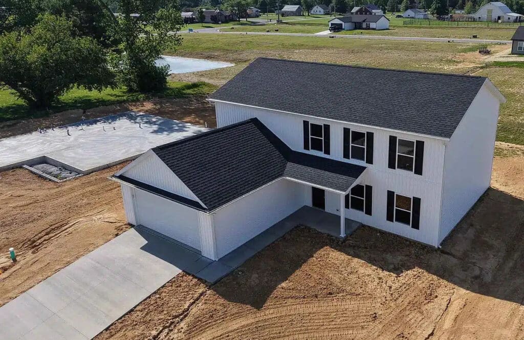 Newly constructed modern house with a spacious driveway and surrounding landscape.